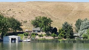 A lakeside property with a dock, a small building, and a hill in the background. - Amazing relaxing get-away home on the Snake River with river view and boat dock. (Hagerman)