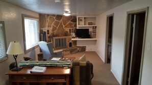 A living room with a stone accent wall, a television, a fireplace, and a cozy seating area. - Amazing relaxing get-away home on the Snake River with river view and boat dock. (Hagerman)