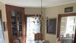 Ein Esszimmer mit einem langen Holztisch, gedeckt für sechs Personen, umgeben von gestreiften Stühlen. Eine Kristallleuchter hängt von der Decke, und links befinden sich Schränke mit Glastüren.