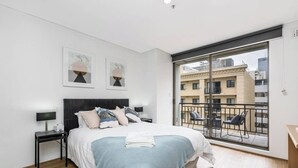 Ein modernes Schlafzimmer mit einem großen Bett, einem Nachttisch, einem Schreibtisch und einem Balkon mit Stühlen.