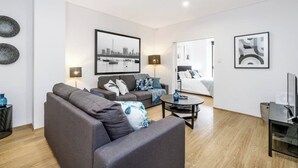 Ein modernes Wohnzimmer mit einem grauen Sofa, einem Couchtisch und einem TV-Schrank. An beiden Seiten des Sofas befinden sich jeweils Lampen.
