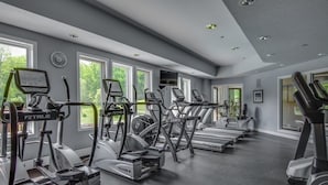 Un gimnasio con múltiples cintas de correr y elípticas, ventanas amplias y una decoración en tonos grises.