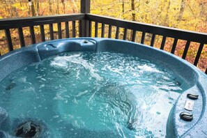 A hot tub with a wooden deck and a view of autumn trees. - Creekside Serenade relax by the running creek (Broken Bow)
