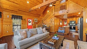 A spacious living area with a wooden ceiling, a sofa, a coffee table, and a kitchen in the background. - Creekside Serenade relax by the running creek (Broken Bow)