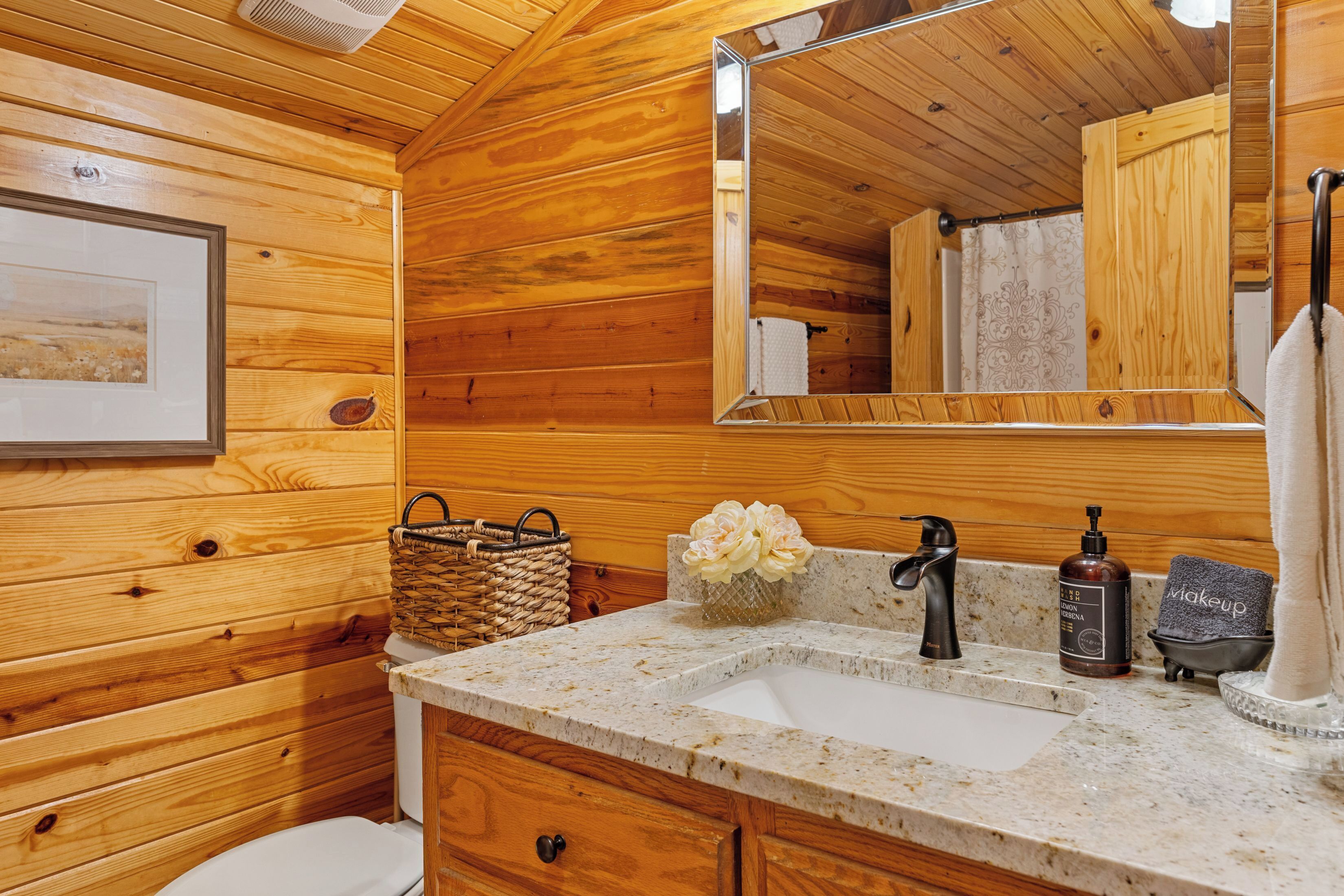 A wooden cabin bathroom with a sink, mirror, and a framed picture on the wall.