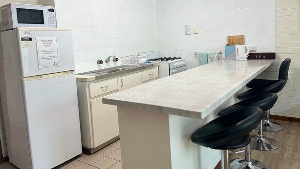 Une cuisine moderne avec des appareils électroménagers blancs, un îlot central doté de tabourets et une bouilloire posée sur le plan de travail.