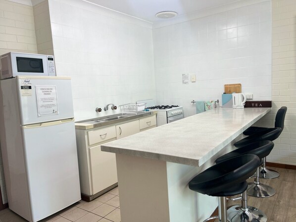 Una cocina moderna con electrodomésticos blancos, una isla central con taburetes altos y un hervidor en la encimera.