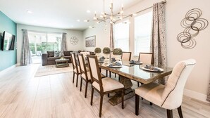 A spacious dining area with a long wooden table, multiple chairs, and a chandelier.