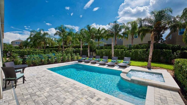 A rectangular swimming pool with a hot tub, surrounded by lounge chairs and a table with chairs.