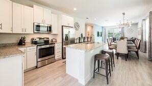 A modern kitchen with stainless steel appliances, a central island, and a dining area with bar stools.