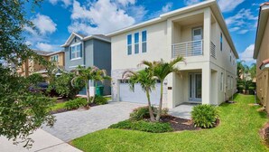 A two-story residential building with a paved driveway, a small lawn, and a palm tree.