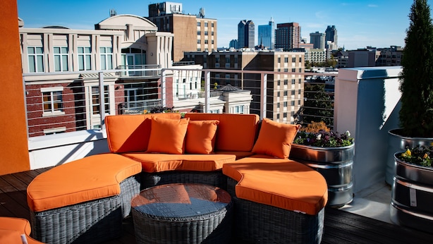 Une terrasse sur le toit, dotée d’un canapé modulable et de fauteuils en osier, offrant une vue panoramique sur la ville et ses bâtiments modernes.