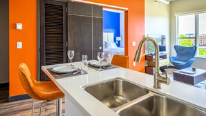 Une cuisine moderne dotée d’un grand îlot central, d’un évier en acier inoxydable et de chaises orange.