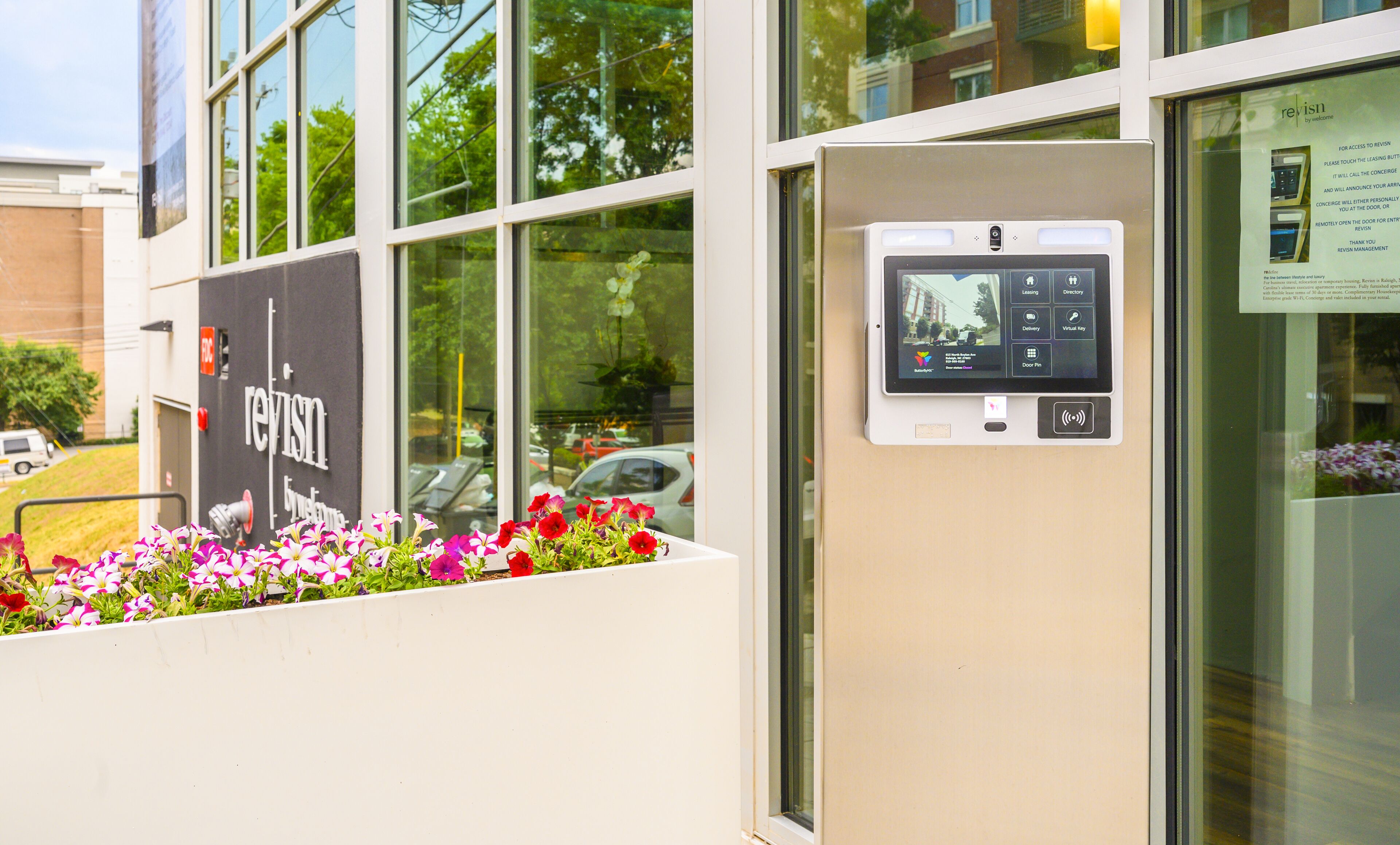 A modern building with a digital kiosk for visitor services, a flower bed with colorful flowers, and a clear view of the street outside.