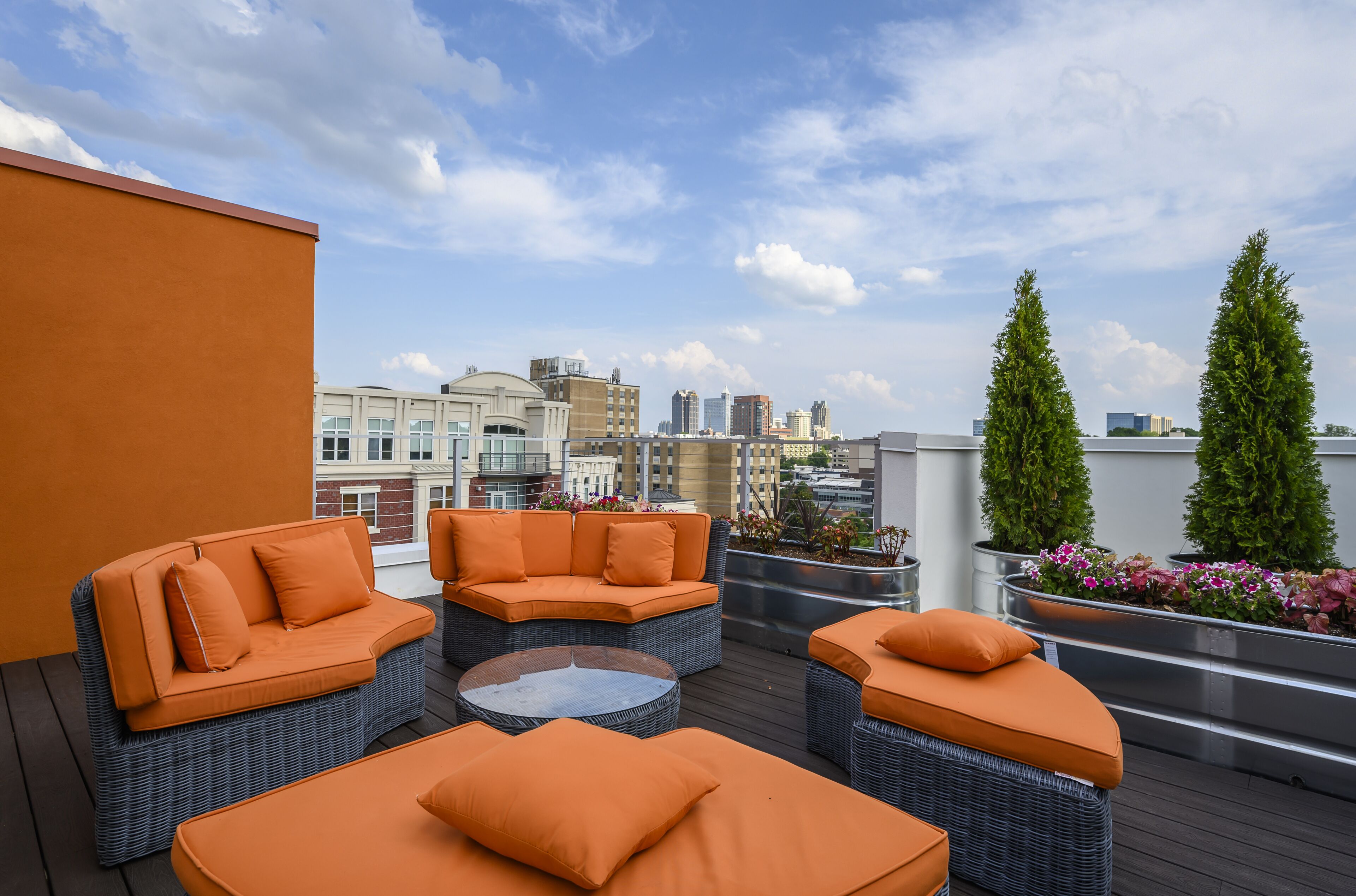 Terraza en la azotea con mobiliario de mimbre y cojines anaranjados, con vistas a un paisaje urbano.