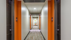Un couloir avec un sol gris et orange, des murs blancs et un plafond foncé.