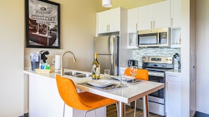 Une cuisine moderne avec des meubles blancs, des appareils en acier inoxydable et un coin bar agrémenté de chaises orange.