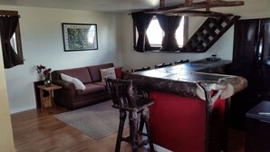 Ein gemütliches Wohnzimmer mit Holzboden, einem braunen Sofa, einem kleinen Beistelltisch mit einer Vase und einer roten Akzentwand.