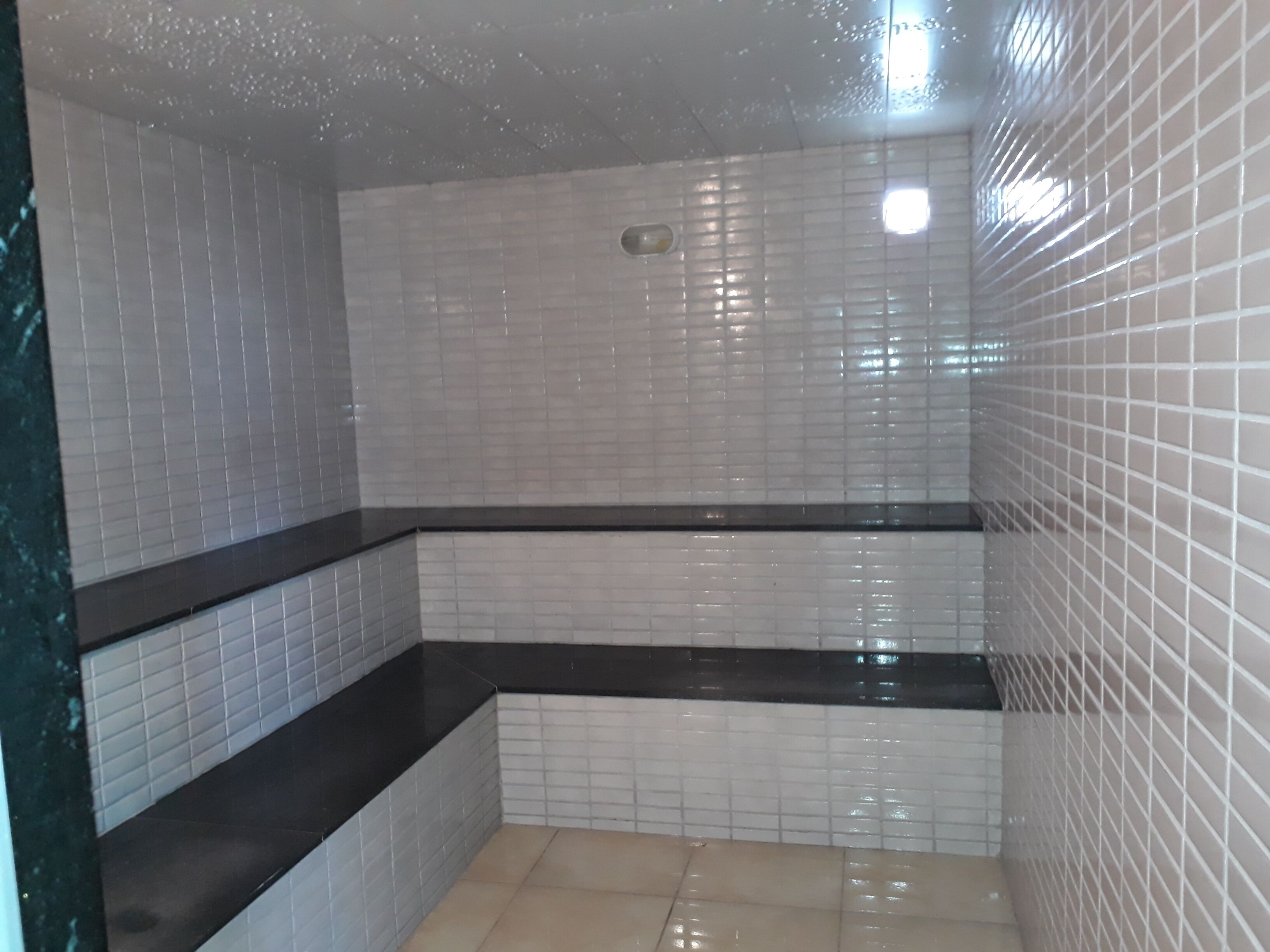 A bathroom with white tiled walls, a black countertop, and a tiled floor.