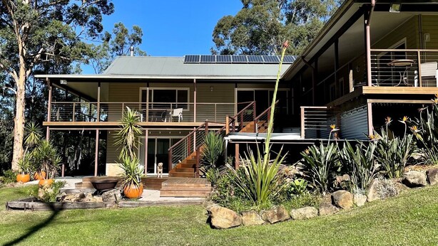 Una casa moderna de dos pisos con balcón, paneles solares y un jardín bien cuidado con diversas plantas y rocas.