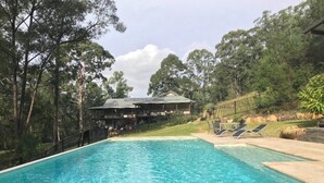 Una piscina con agua cristalina, rodeada de árboles y un edificio con techo.