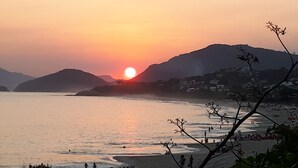 Un coucher de soleil sur la côte, avec une plage et des collines en arrière-plan.