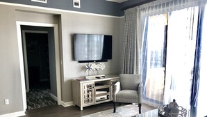 A modern living room with a flat-screen TV, a comfortable armchair, a glass coffee table, and a patterned rug.