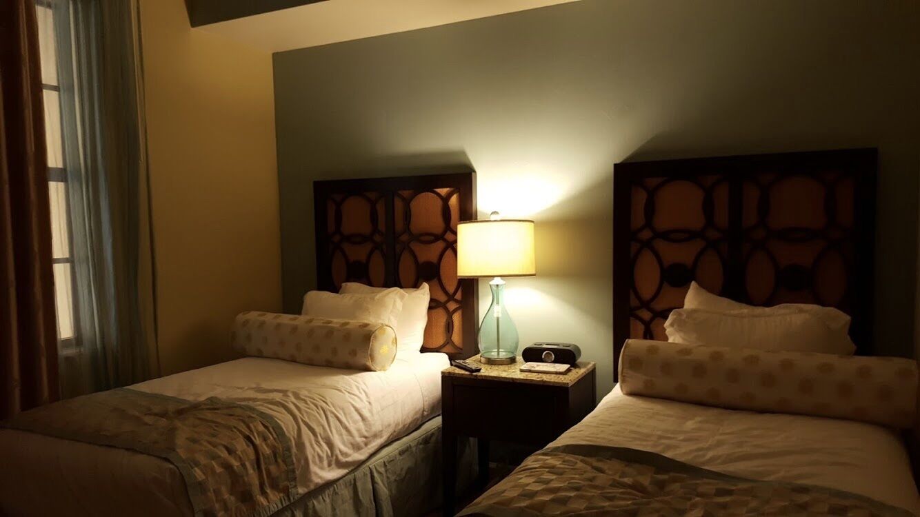 A hotel room with two beds, a nightstand with a lamp, and a decorative headboard.