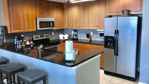 A modern kitchen with wooden cabinets, a central island, stainless steel appliances, and a bar area.