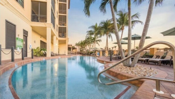 A pool area with a curved design, palm trees, and lounge chairs.