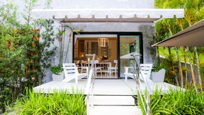A modern outdoor seating area with white chairs and a table, surrounded by lush greenery and a clear view into the building. - 5 star BEACH SIDE LUXURY APARTMENT/CHEF SERVICE BKFAST (Las Terrenas)