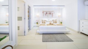 A modern bedroom with a large bed, bedside tables, a hanging light fixture, and a view of the bathroom. - 5 star BEACH SIDE LUXURY APARTMENT/CHEF SERVICE BKFAST (Las Terrenas)