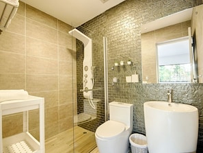 Un baño moderno con ducha, inodoro y lavabo, que cuenta con un revestimiento de pared de piedra y un espejo grande.
