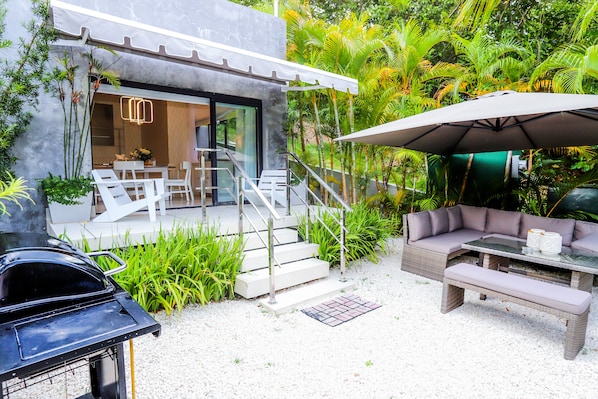 Un patio exterior moderno con zona de comedor, una parrilla y un área de estar con mesa y sillas.