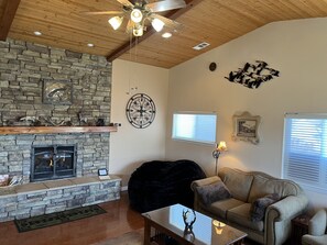 A living room with a stone fireplace, a ceiling fan, and a couch. -  LUXURY LAKE HOUSE  & TREEHOUSE DAYBED 5-STAR QUALITY- Plush beds for 10    (Julian)