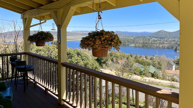 A wooden deck with hanging flower pots and a view of a lake and mountains.