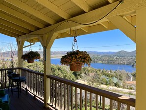 A wooden deck with hanging flower pots and a view of a lake and mountains.