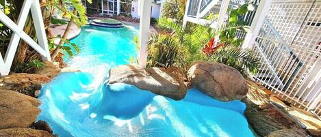 Ein Pool mit steinverkleideter Kante, umgeben von einem weißen Zaun und viel Grün.