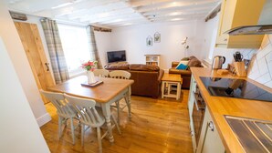 A cozy living room with a wooden dining table, white chairs, a brown sofa, and a television.