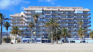 Ein mehrstöckiges Hotel mit Balkonen, Palmen und einem Sandstrand im Vordergrund.