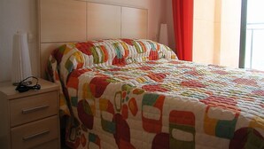 Ein Schlafzimmer mit Bett, Nachttisch, Lampe und einem Fenster mit Vorhängen.