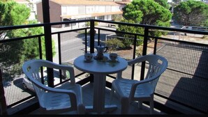 Un balcon avec deux chaises en plastique blanc et une petite table ronde, sur laquelle se trouvent une cafetière et des tasses.