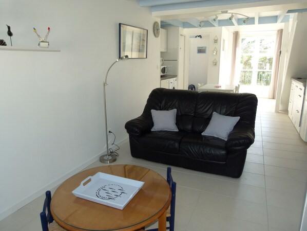 A living room with a black leather sofa, a wooden coffee table, and a dining area with a small table and chairs.