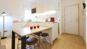 A modern kitchen with white cabinets, a wooden countertop, and a coffee machine. There are three stools at the counter. - Charming Malasaña (Madrid)