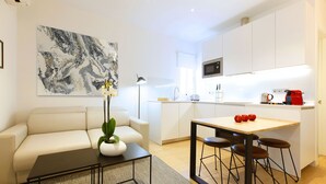 A modern kitchen with white cabinets, a wooden dining table with bar stools, a white sofa, and a coffee machine. - Charming Malasaña (Madrid)