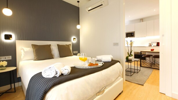 A modern hotel room with a neatly made bed, a breakfast tray, and a view into the kitchen area. - Charming Malasaña (Madrid)