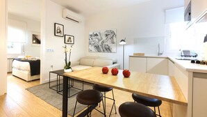 A modern, well-lit room with a wooden dining table, black chairs, a white sofa, and a kitchen area. - Charming Malasaña (Madrid)