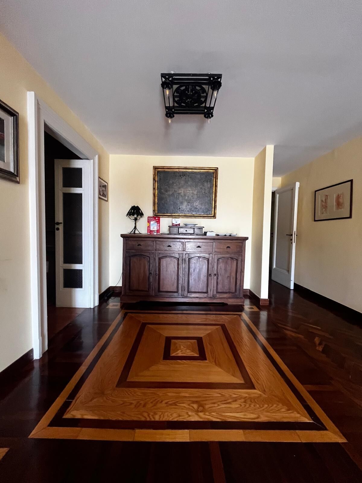 A hallway with a wooden floor, a dark wooden cabinet, and a ceiling light fixture.