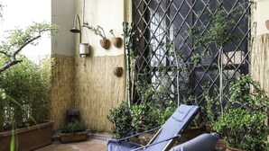 Un pati il·luminat pel sol amb una cadira relaxant, plantes en testos i una paret de bambú.