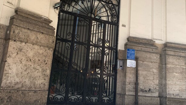 Entrada d'un edifici amb una gran porta de ferro negre, columnes de pedra i un sòl de rajoles.